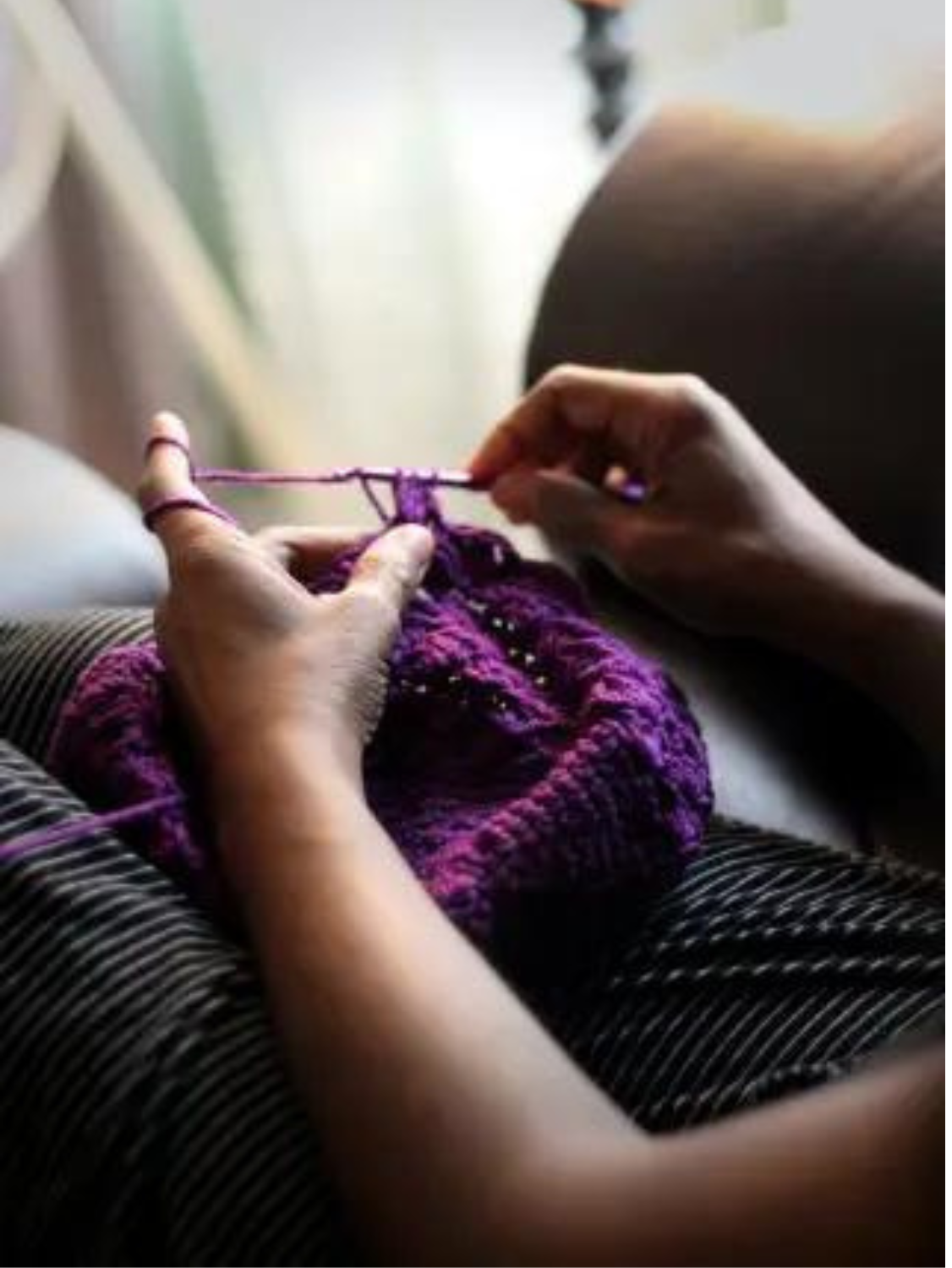 A woman reclines on a couch, working with a crochet hook and purple yarn.